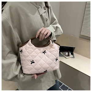 Detailed shot of pink quilted handbag with black bow embroidery and dark brown leather handles