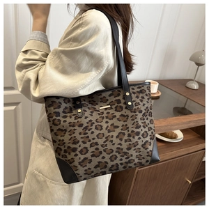 Detail of leopard print tote bag featuring a gold metal logo and black leather corners