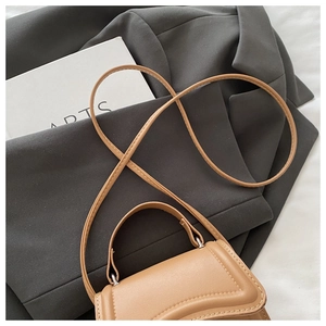 Detail of a brown leather mini bag with curved flap and fine stitching on a blazer