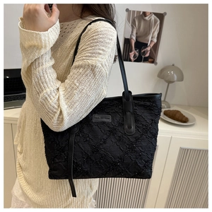 Detail of black textured tote bag with shimmering rhombic patterns and leather logo patch