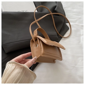 Close-up of a micro brown leather handbag held against a grey suit and white fabric