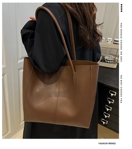 Detail of a large brown faux leather tote bag carried by a model in a cozy indoor setting