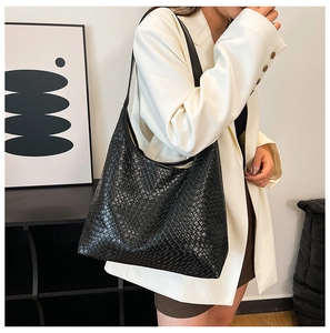 Detail of black woven texture tote bag worn over the shoulder by a woman in casual attire