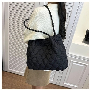 Detail of black quilted shoulder bag with puffy diamond texture and woven straps