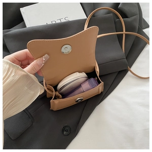 Detail view of brown leather crossbody bag interior holding cosmetics on a grey blazer