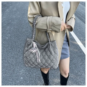 Detail of grey quilted tote bag with braided handles and plush charm in outdoor setting