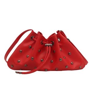 Red drawstring bucket bag with metal rivets and thin leather shoulder strap on white base