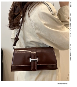 Deep brown glossy leather baguette bag with silver buckle worn on a shoulder