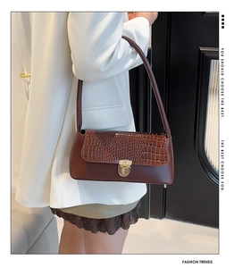 Close-up of brown baguette bag featuring crocodile pattern flap and gold clasp