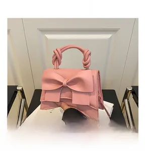 Close-up of pink crossbody bag with large bow detail and woven handle on a black chair