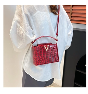 Detail of red croc-embossed bucket bag featuring gold V-shaped metal hardware and strap