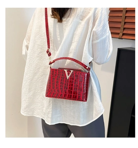 Street style view of a red croc-textured bucket bag with silver V-shaped buckle