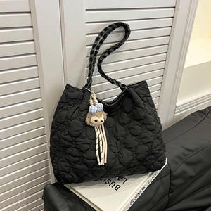 Quilted black tote bag with woven handles and plush charm in a modern room setting