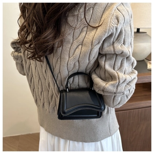 Detail of a black textured crossbody bag styled with a beige knit sweater and long white skirt
