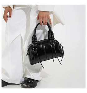 Close-up of black glossy leather pillow bag with silver eyelets and long fringe tassels