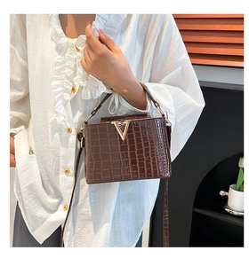 Detail shot of brown crocodile pattern bag featuring a golden V-shaped metal clasp