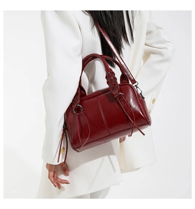 Detail of burgundy glossy leather handbag with braided handle and long tassels