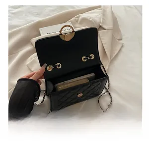 Detail view showing internal storage of black quilted bag with gold chain and phone