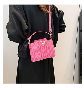Detail of rose red crocodile pattern handbag with golden metal V buckle and top handle