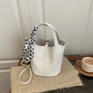 Elegant white bucket bag with pebble texture and polka dot scarf detail on table