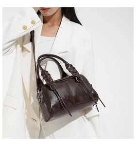 Detail of dark brown glossy leather Boston bag featuring woven handles and stylish tassels