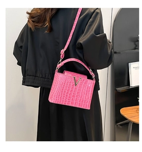 Detailed side view of pink crocodile pattern bucket bag with V-shaped metal logo and strap