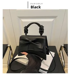 Detail view of the black crossbody bag featuring a large bow and knotted top handle