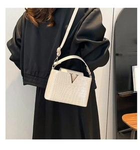 Detail of cream crocodile texture leather bucket bag with gold V-buckle and top handle
