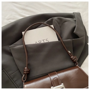 Dettaglio borsa vintage marrone scuro con fibbia a H argentata su blazer grigio