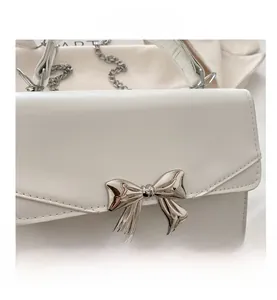 Detailed close-up of the silver mirror metal bow and white faux leather bag texture