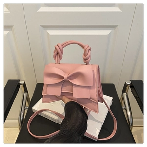 Détail du sac à main rose avec grand nœud et poignée torsadée tenu par la main