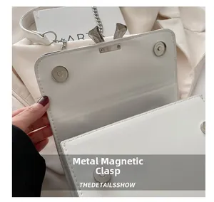 Detailed close-up of the silver magnetic clasp on a white leather flap handbag