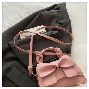 Détail d'un sac bandoulière rose avec nœud et poignée nouée sur fond de veste de costume douce