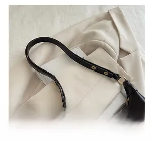 Close-up of black crescent underarm bag with gold hardware on a beige blazer