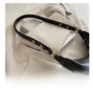 Detail of dark leather crescent bag with gold metal buckle and adjustable studs