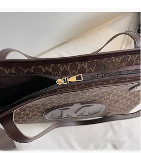 Detailed close-up of smooth gold metal zipper and logo print on dark brown tote bag