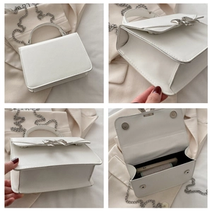 Detail view of white square bag showing silver bow decor, chain strap and interior space