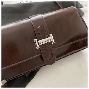 Dettaglio della borsa in pelle lucida marrone scuro con fibbia metallica rettangolare