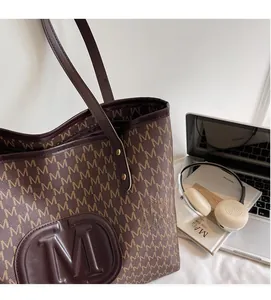 Macro shot of brown tote bag featuring embossed M pattern and matching commute accessories