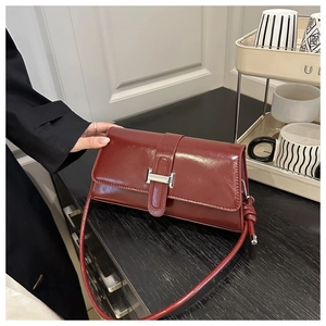 Detail of burgundy leather shoulder bag with a silver H-shaped buckle in hand