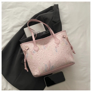 Dettaglio della borsa tote rosa con ricami e coulisse posata su un blazer grigio