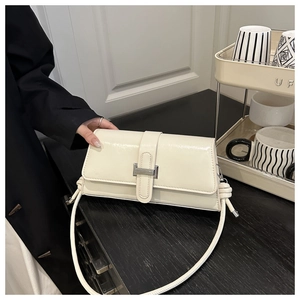 Detail of cream-white leather baguette bag with elegant metal buckle and knotted strap