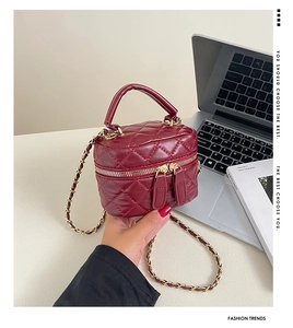 Close-up of burgundy quilted bucket bag with gold chain strap and dual zipper detail