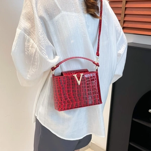Red crocodile texture bucket bag with gold V-hardware shown on model from side view