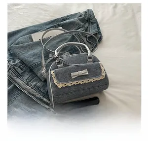 Détail d'un sac en denim avec nœud argenté et dentelle blanche dans un décor décontracté