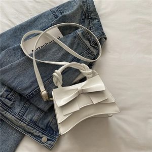 Sac à main chic en cuir blanc avec grand nœud et poignée torsadée sur fond de denim
