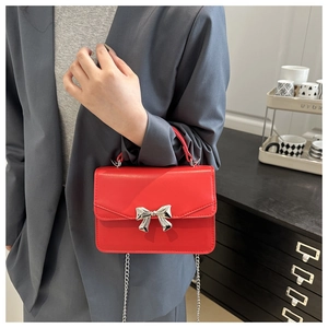Close-up of bright red crossbody bag with silver bow buckle and metallic chain strap