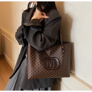 Close-up of brown tote bag with M-monogram pattern and embossed logo detail