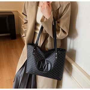 Detail shot of black tote bag with letter M monogram pattern and logo on a model
