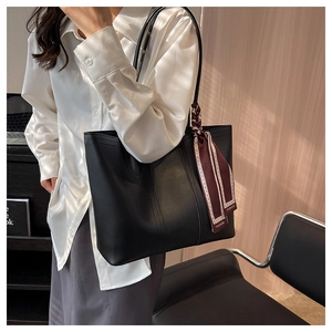 Detail of black leather tote bag with elegant burgundy floral scarf on a strap